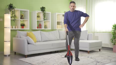 Mature-man-sweeping-carpet-in-modern-living-room,-cleaning-with-vacuum-cleaner.